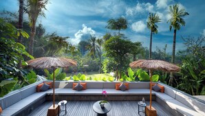 Un salon sur le toit doté d’une terrasse en bois, de sièges confortables et de deux parasols en chaume.