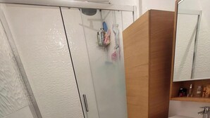 Kylpyhuoneessa on lasiseinäinen suihkukaappi, puinen allaskaappi ja peili pesualtaan yläpuolella.