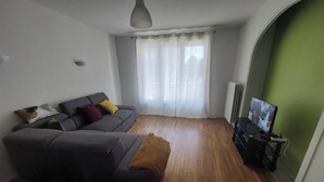 Olohuone, jossa on harmaa sohva, ruskea huopa, televisio ja patteri.