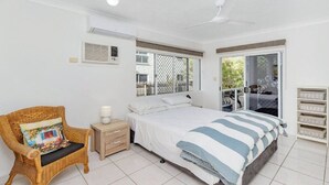 Une chambre à coucher comprenant un lit, une chaise, une table de chevet, une fenêtre avec vue et un ventilateur de plafond.