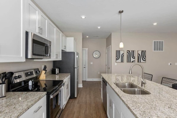 A modern kitchen with white cabinets, stainless steel appliances, granite countertops, and a built-in dishwasher.