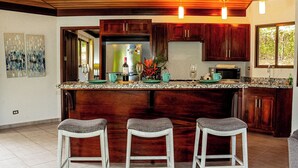 A kitchen with wooden cabinets, a granite countertop, and three bar stools. - 3 bedrooms. Large pool. Gated. Private. Ojochal. (Ojochal)