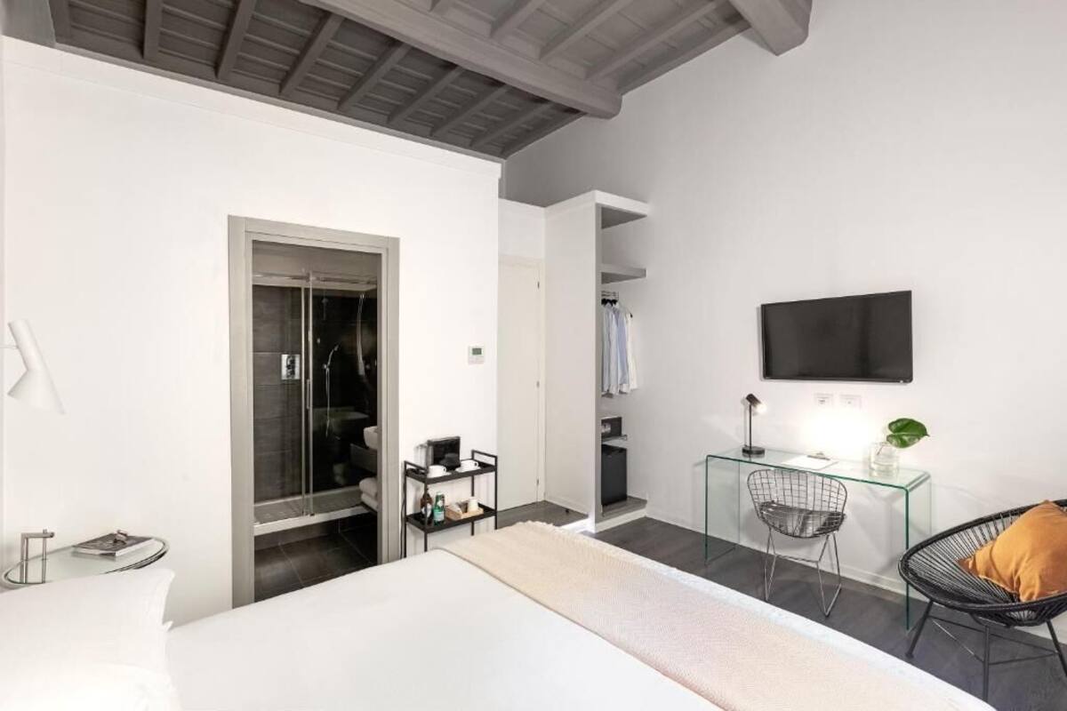 A modern hotel room with a bed, a glass desk, a chair, a TV, and a walk-in closet.