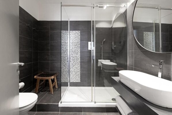 A modern bathroom with a glass-enclosed shower, a white bathtub, and a small wooden stool.