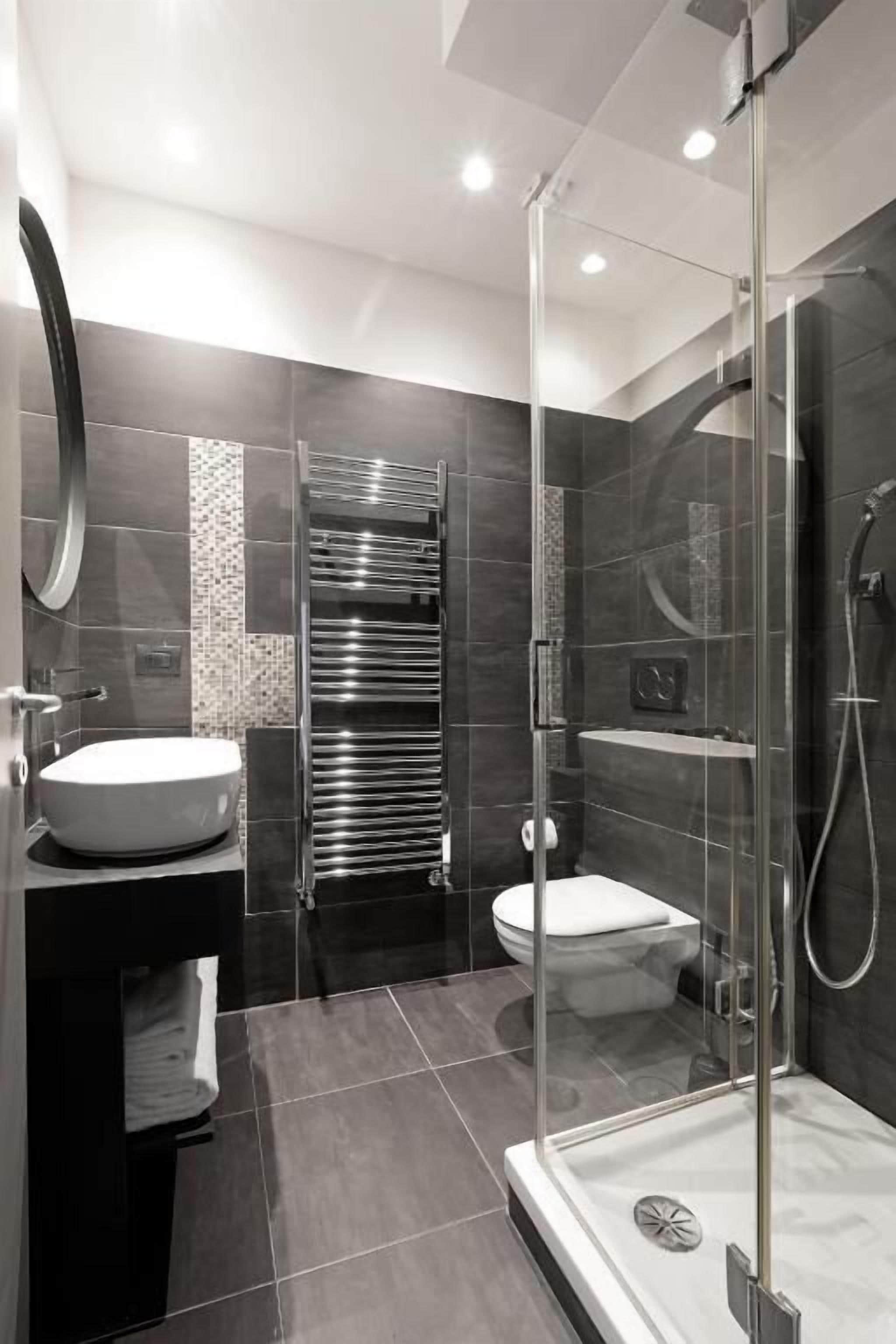 Un baño moderno con ducha de vidrio, lavabo redondo y retrete.