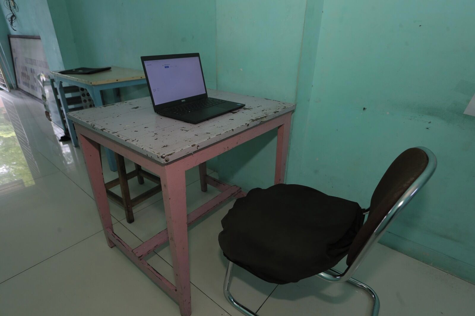 Een kleine kamer met een laptop op een tafel, een stoel en een whiteboard aan de muur.