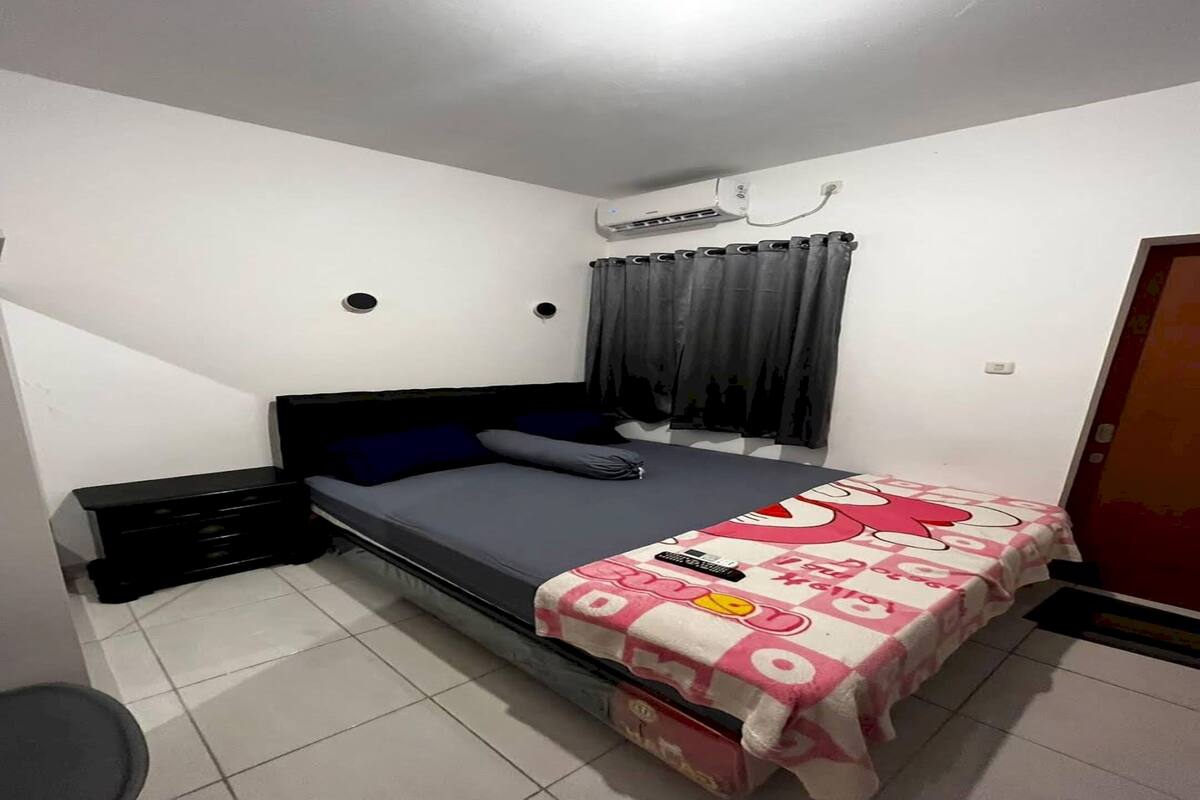 Ein Schlafzimmer mit einem Einzelbett, einem Nachttisch, einer Kommode, einem Fenster mit Vorhängen und einer Klimaanlage.
