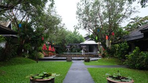 A pathway leading to a covered seating area surrounded by lush greenery and potted plants. - Vimarn Kaew Village and Resort (Chiang Mai)