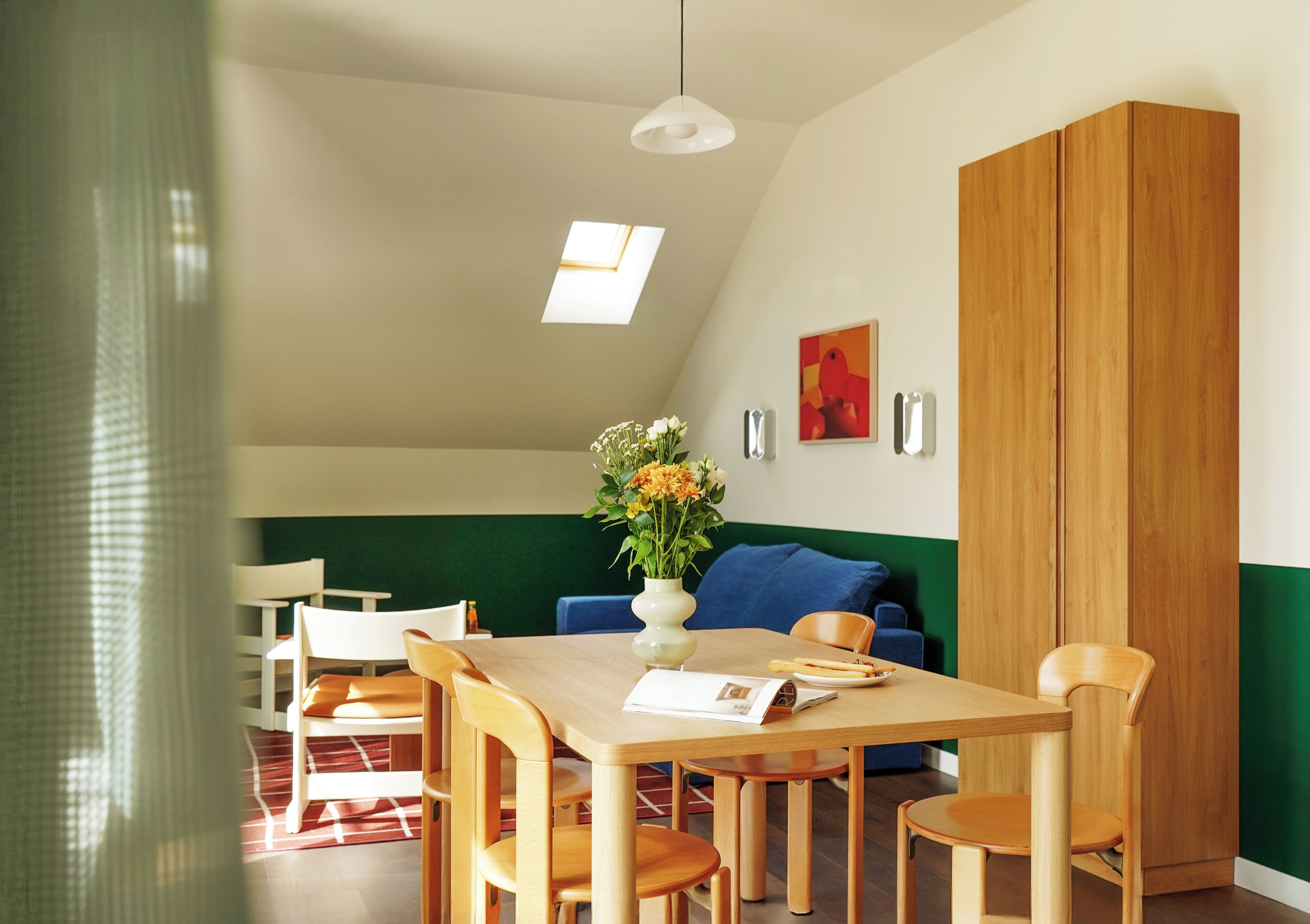 A dining area with a wooden table, chairs, a vase with flowers, and a blue sofa.