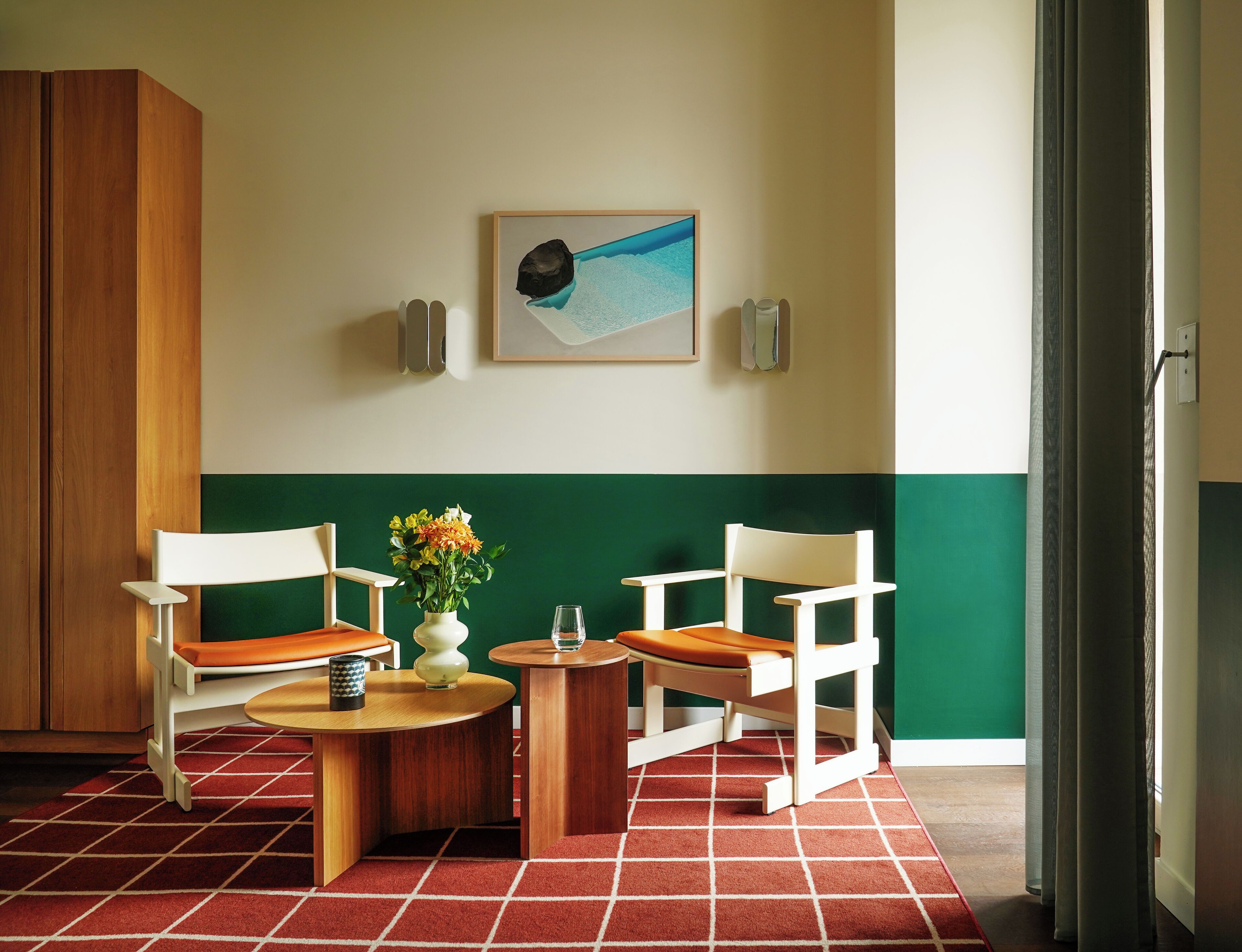Une pièce avec deux chaises blanches, une table en bois, un vase avec des fleurs et un tableau au mur.