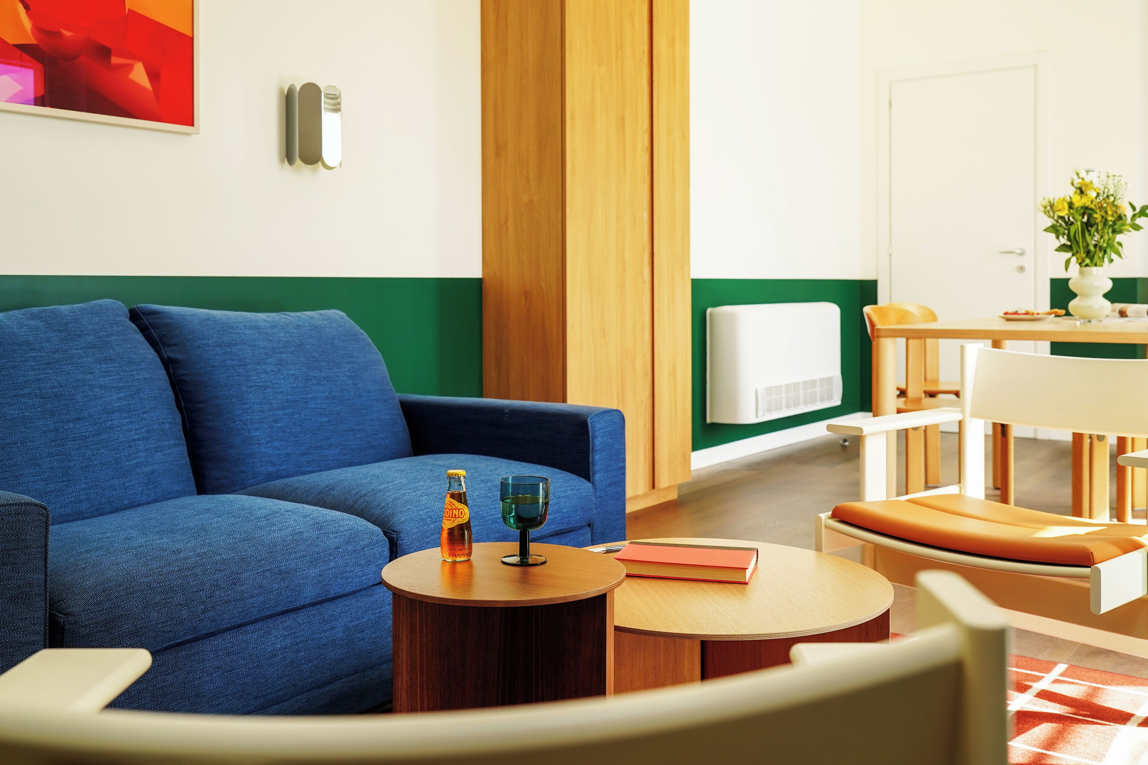 Ein modernes Wohnzimmer mit einem blauen Sofa, einem runden Holztisch und einem Essbereich mit einem weißen Tisch und Holzstühlen.