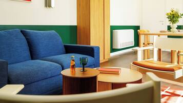 Ein modernes Wohnzimmer mit einem blauen Sofa, einem runden Holztisch und einem Essbereich mit einem weißen Tisch und Holzstühlen.