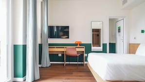 Une chambre d’hôtel avec un lit, un bureau, une chaise et une grande fenêtre avec des rideaux.