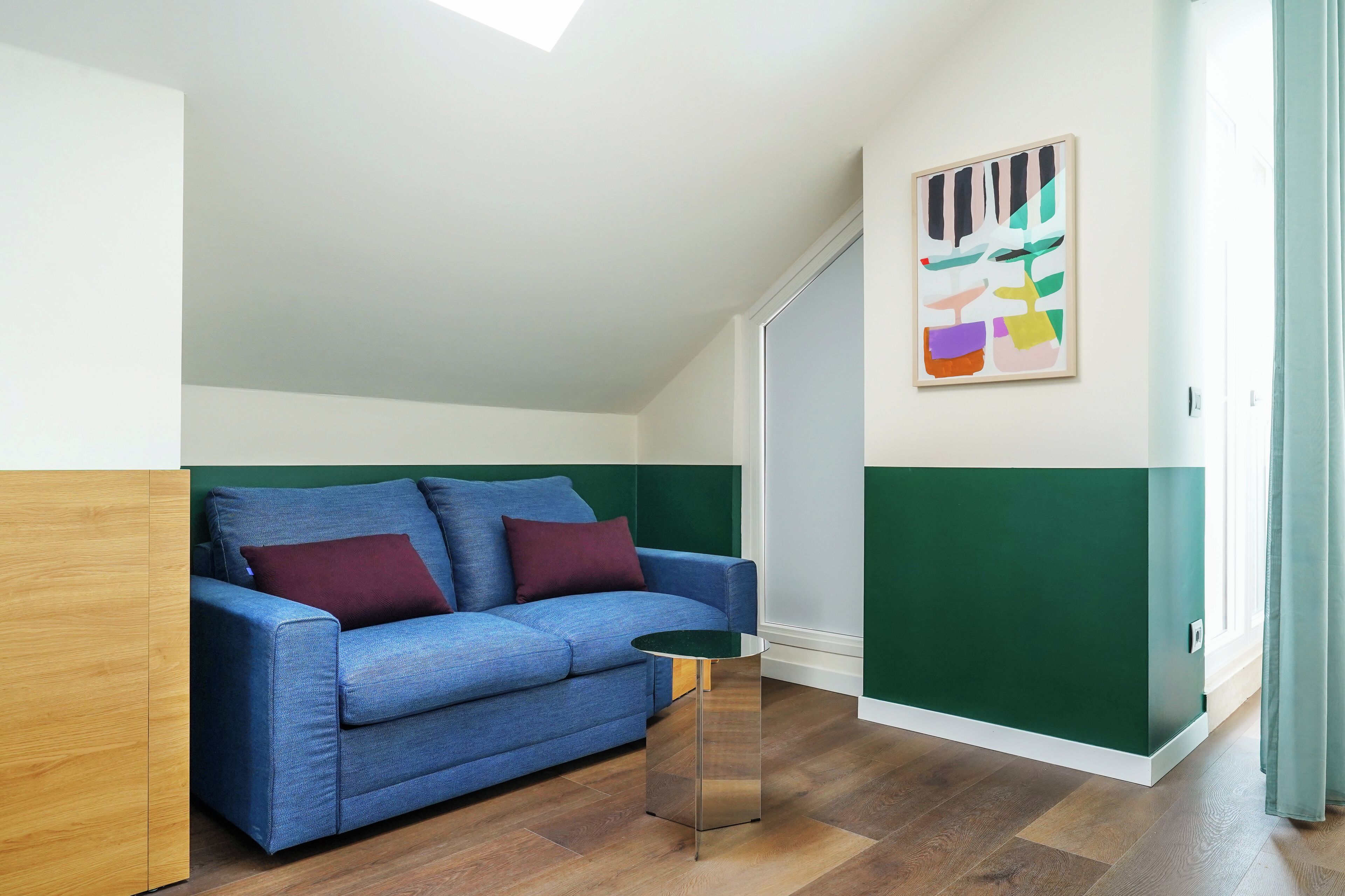 Une pièce avec un canapé bleu, une petite table ronde et un tableau abstrait aux couleurs vives accroché au mur.