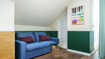 Une pièce avec un canapé bleu, une petite table ronde et un tableau abstrait aux couleurs vives accroché au mur.