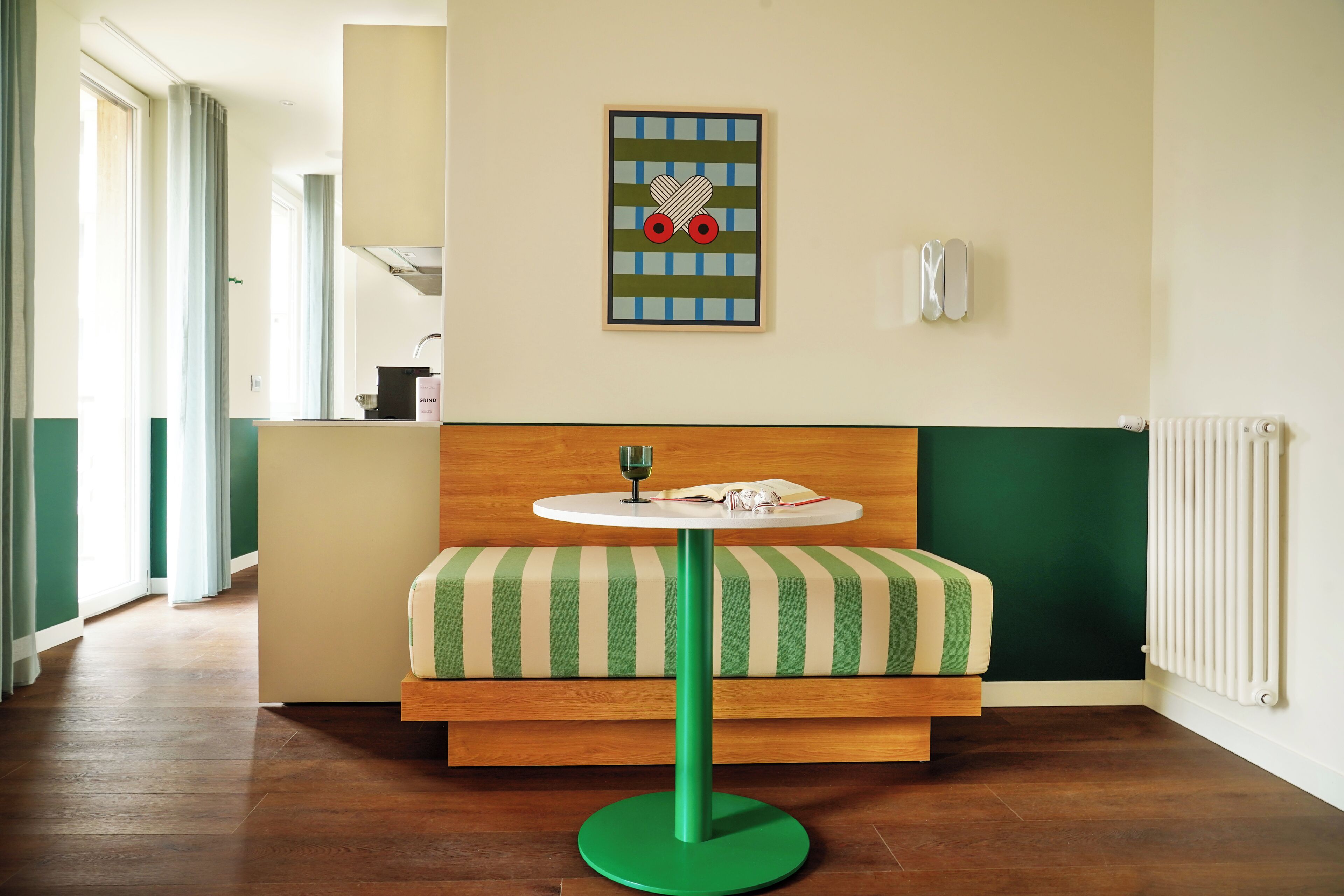 Ein Zimmer mit einem grün gestreiften Sofa, einem runden Tisch mit einem Glas und einem an der Wand hängenden Kunstwerk.