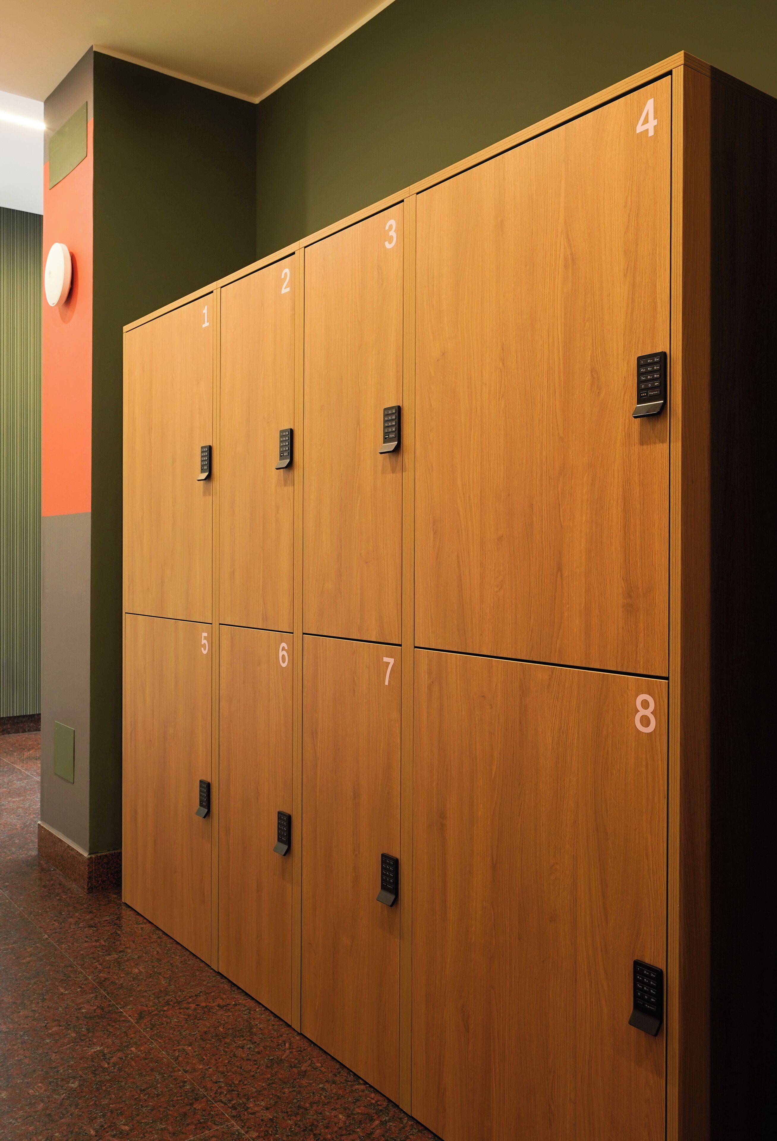 A row of wooden lockers numbered 1 to 8 in a hallway with green walls and a red accent wall.