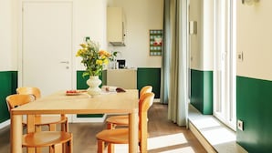 Un coin repas avec une table et des chaises en bois, un vase de fleurs et, au fond, une cuisine.