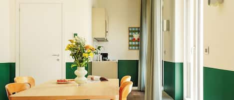 A dining area with a wooden table and chairs, a vase of flowers, and a kitchen in the background.