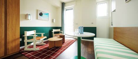 Una habitación de hotel con una cama, una mesa redonda, una silla, una mesita auxiliar y una alfombra roja.
