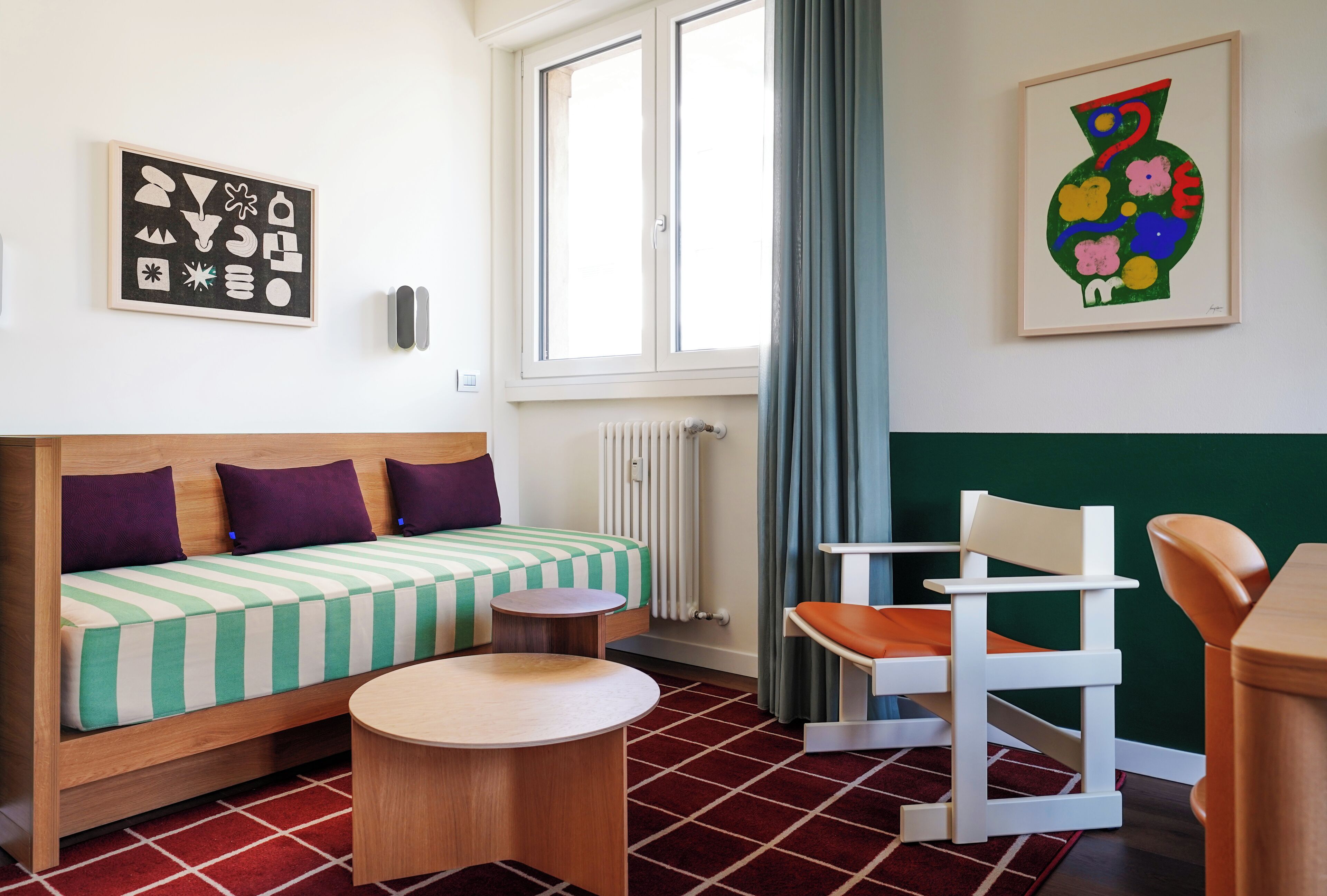 A room with a bed, a chair, a small table, and artwork on the walls.
