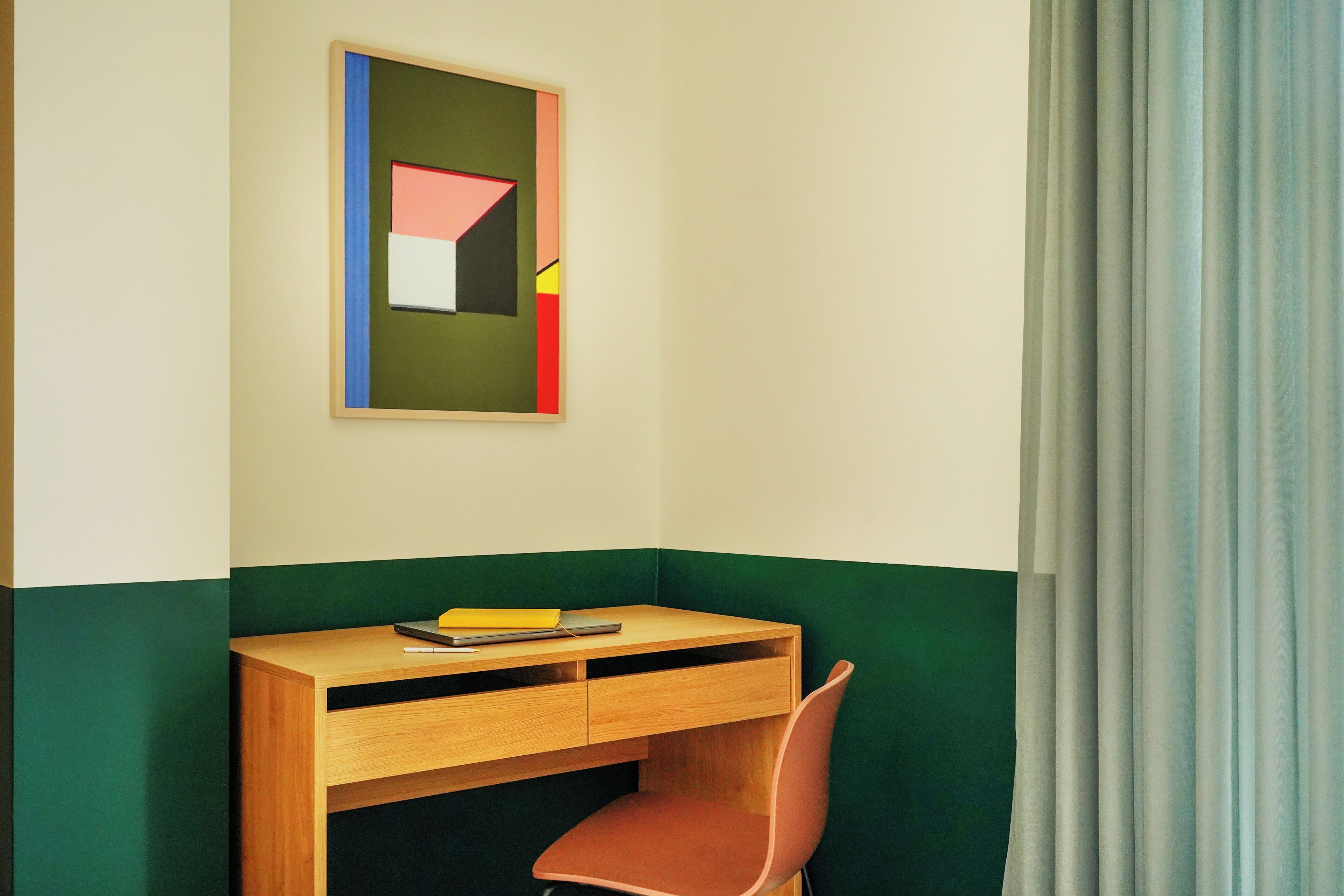 A corner room with a desk, chair, and a framed abstract painting on the wall.