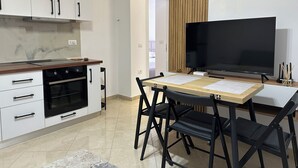 A modern kitchen with white cabinets, a black oven, and a wooden countertop. There is a dining table with black chairs and a large flat-screen TV. - Cobalt Apartments. 1-bedroom apartment in Vlora. (Vlora)