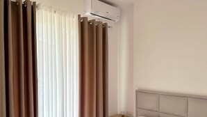 A hotel room with a bed, white curtains, a nightstand with a glass, and an air conditioning unit. - Cobalt Apartments. 1-bedroom apartment in Vlora. (Vlora)