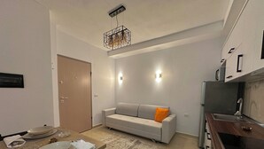 A modern kitchen with a dining area, featuring a sofa, a wooden dining table set with plates, and a kitchen island with a sink. - Cobalt Apartments. 1-bedroom apartment in Vlora. (Vlora)