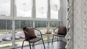 A modern room with large windows, two chairs, a small table with a fruit bowl, and a bottle.