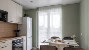 A modern kitchen with white cabinets, a built-in oven, and a refrigerator. There is a dining table set with plates, cups, and a vase with flowers.