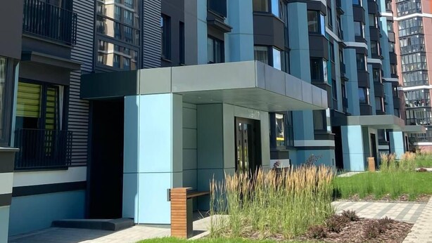 A modern multi-story residential building with balconies, a covered entrance, and a well-maintained lawn area.