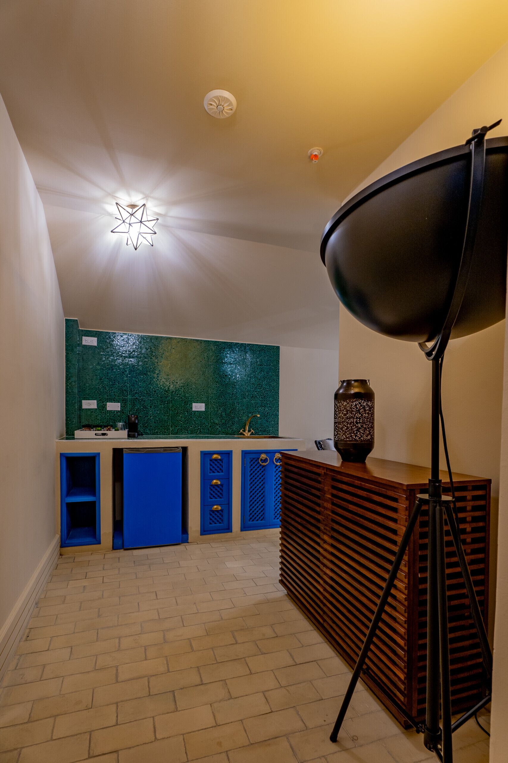 A modern kitchen with blue cabinets, a green backsplash, and a black floor lamp.