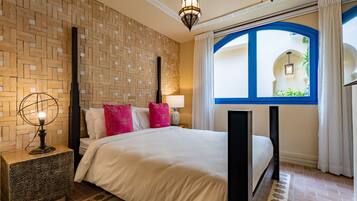 Een verzorgde slaapkamer met een groot bed, een nachtkastje, een lamp en een raam met uitzicht op groen.