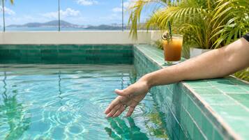 A hand reaching into a pool with a clear view of the sky and distant mountains.