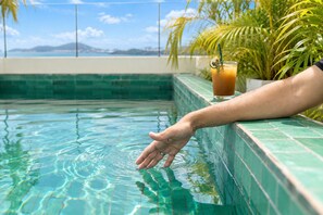 Mão alcançando a água de uma piscina, com vista clara do céu e montanhas ao longe.