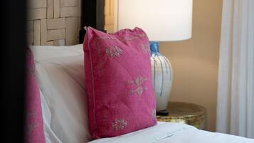Un letto con lenzuola bianche e un cuscino rosa, una lampada su un comodino e un motivo decorativo intrecciato al muro.