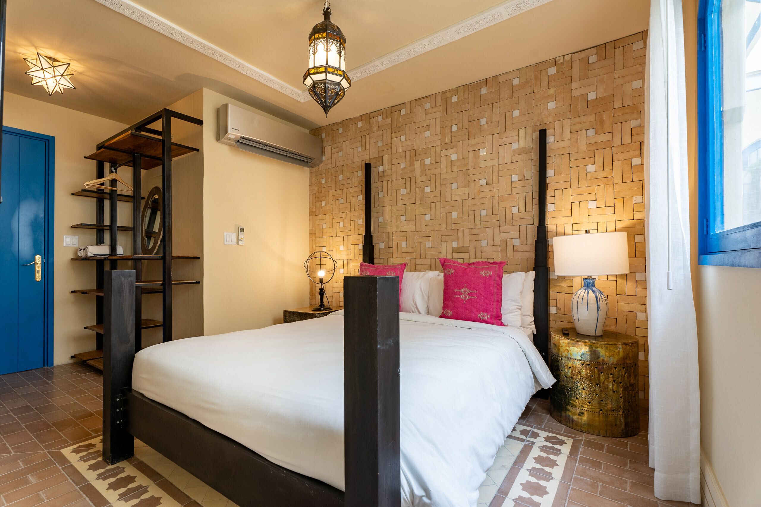 A hotel room with a bed, a nightstand, a lamp, a wardrobe, and a hanging light fixture.