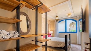 A hotel room with a bed, wooden shelves, a mirror, and a view of the outside through a window with blue framing. - Superior room with communal pool Ma10 (Ciudad de Panamá)