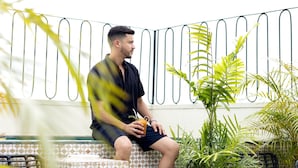 A man sitting on a tiled bench outdoors, holding a drink, with potted plants and a metal fence in the background. - Balcony Superior with communal pool Ma8 (Ciudad de Panamá)