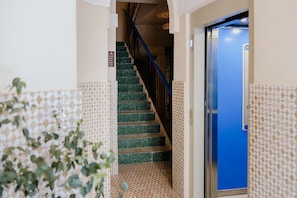 Un escalier recouvert de carreaux verts mène à une porte bleue, le tout étant encadré de murs ornés de motifs.