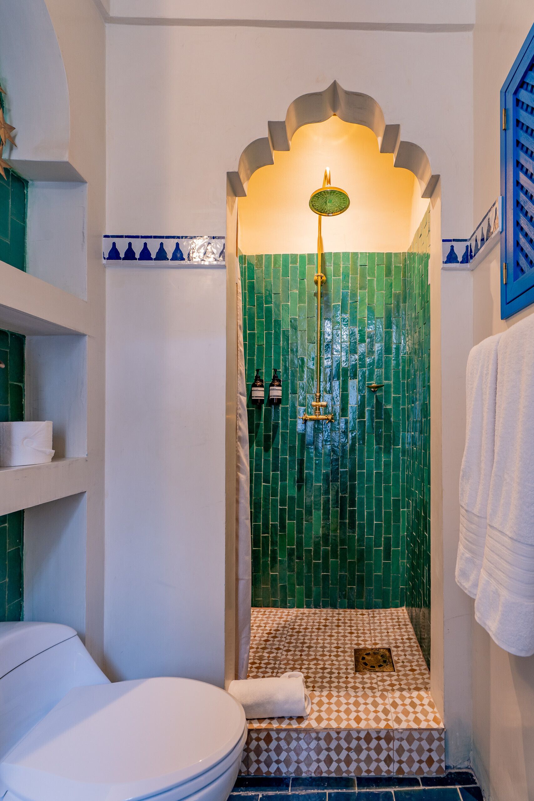 Een badkamer met een douche met groene tegels, een wit toilet en een handdoekrek.