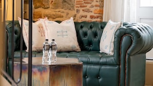 Un canapé en cuir vert agrémenté de coussins décoratifs, une petite table d’appoint avec deux bouteilles, et un mur en pierre en arrière-plan.