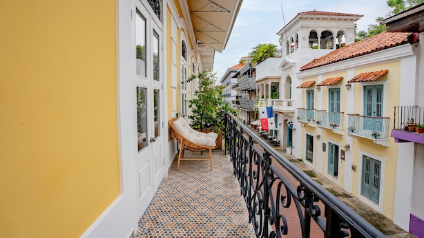 Une ruelle étroite avec un sol carrelé, une chaise en osier et un balcon doté d’une balustrade.