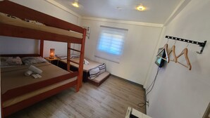A compact room with bunk beds, a small bedside table with a lamp, a window with blinds, and a TV mounted on the wall. - Camp Rofelio Surfing Beach Resort (San Felipe)