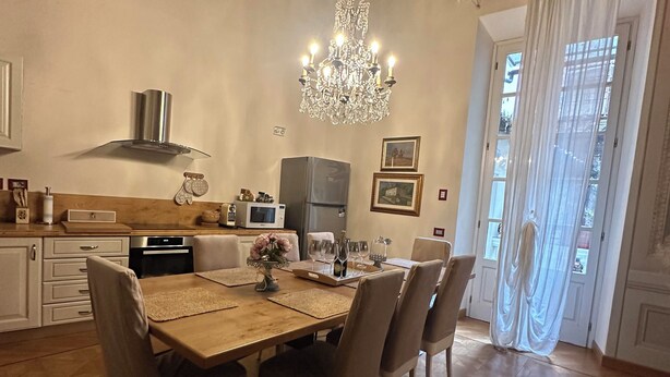 A dining area with a wooden table, chairs, a chandelier, a refrigerator, and a kitchen in the background. - In Center Lucca Lovely Home (Lucca)