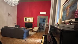 A living room with a piano, a red wall, a chandelier, and a painting. - In Center Lucca Lovely Home (Lucca)