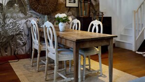 A dining area with a wooden table and white chairs, surrounded by a large decorative wall with palm leaves and framed pictures. - La Hunière Belle Maison Pour 6 Personnes (Barneville-Carteret)