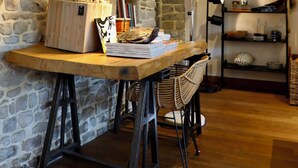 A rustic room with a stone wall, wooden beams, a wooden desk with a lamp, a chair, and a bookshelf. - La Hunière Belle Maison Pour 6 Personnes (Barneville-Carteret)