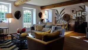 A spacious living room with a large sofa, a coffee table with flowers, and a dining area with chairs. - La Hunière Belle Maison Pour 6 Personnes (Barneville-Carteret)